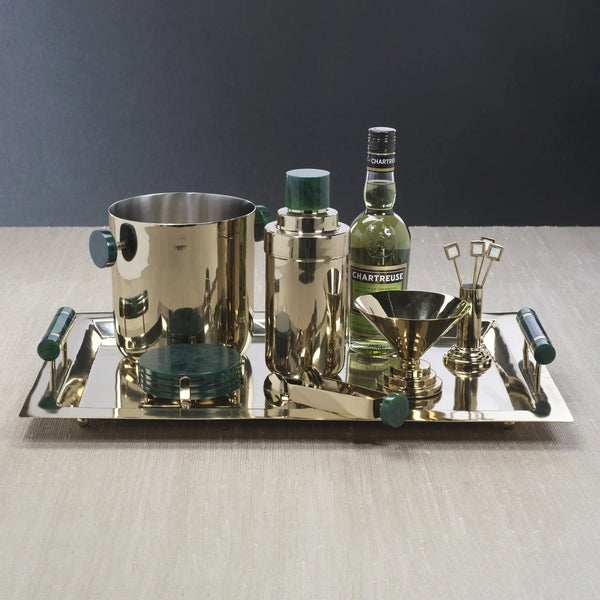 The Spector Serving Tray by Zodax, featuring gold and green marbled handles, holds barware staples—ice bucket, cocktail shaker, Chartreuse bottle, gold jigger and funnel, bar tools, and a green marble coaster—on a light wood surface.