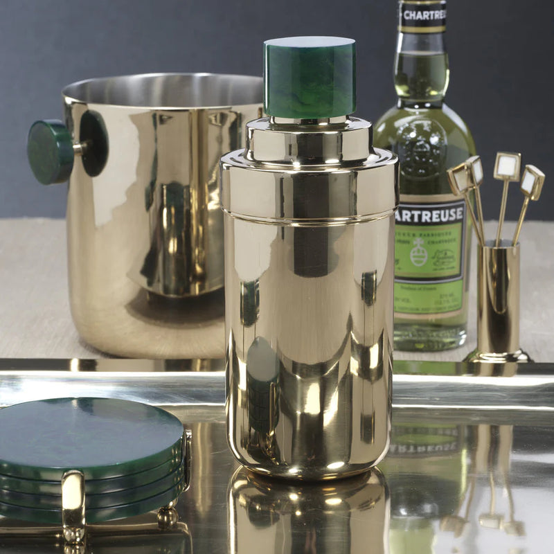 The Zodax Spector Cocktail Shaker in gold and green is displayed on a tray with matching gold barware, a bottle of Chartreuse, green coasters, and a gold ice bucket featuring green handles.