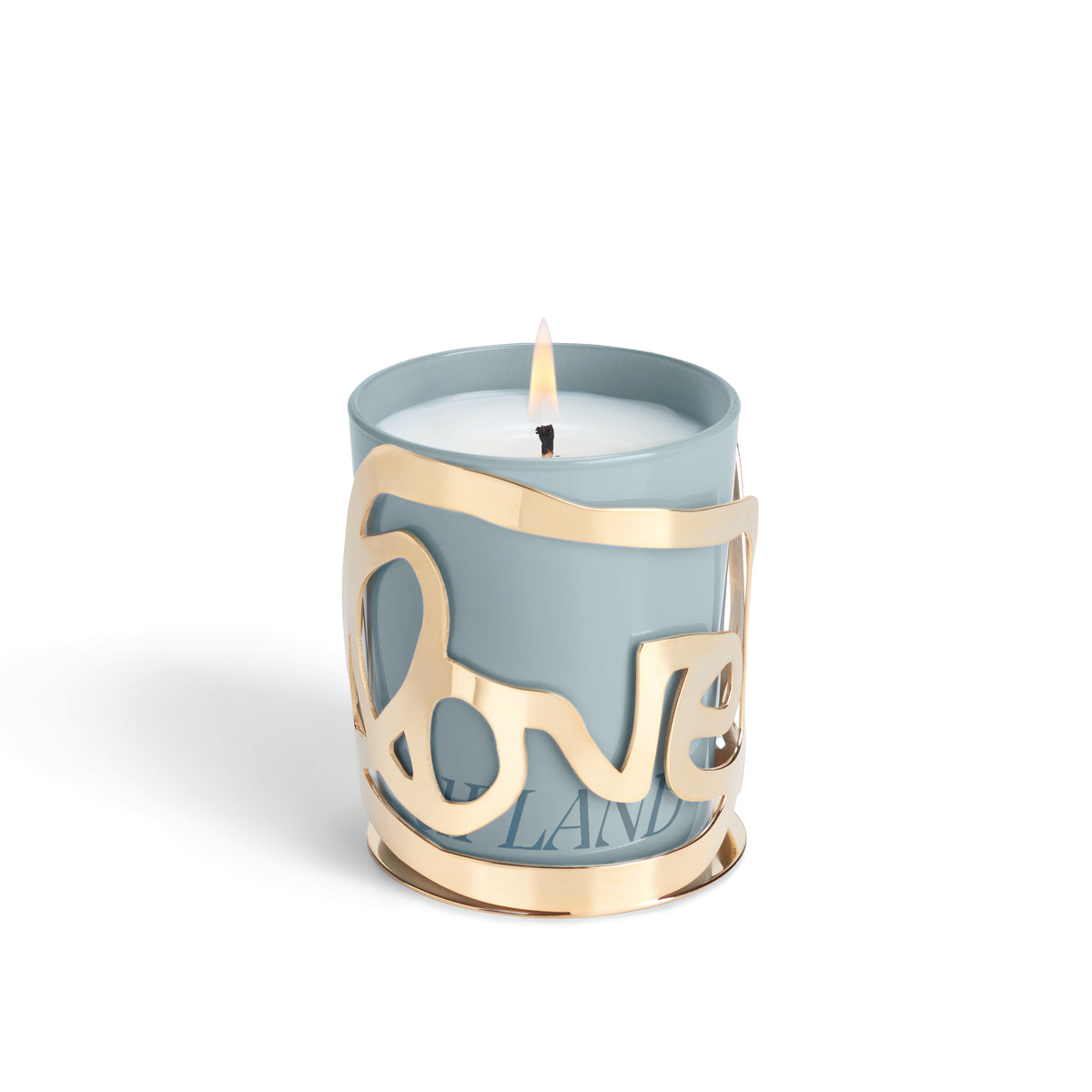 The Love Candle - Upland by Amber Sakai features a lit white candle in a light blue holder, adorned with a decorative gold metal sleeve that spells “LOVE” in elegant cursive letters.