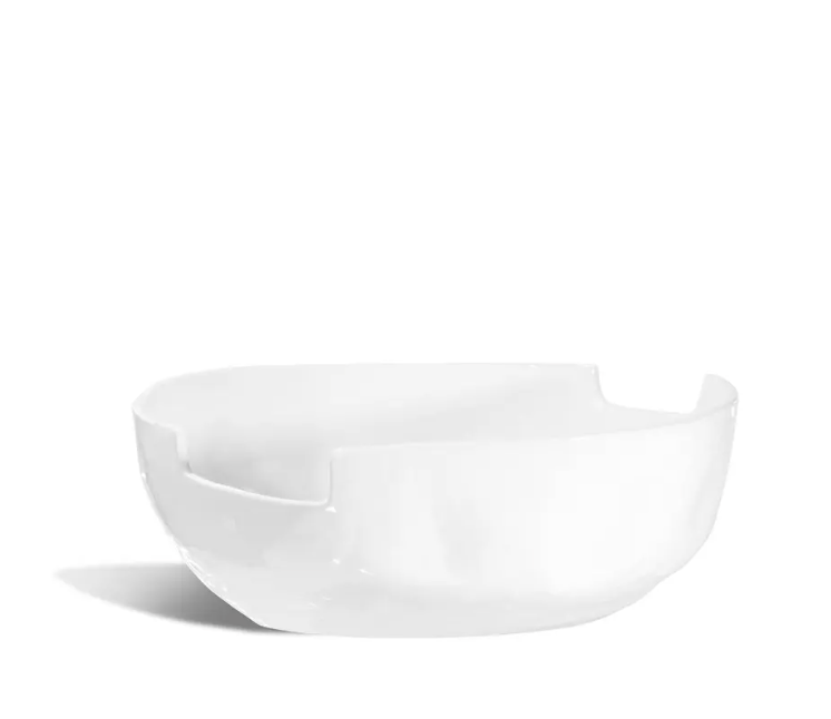 The Montes Doggett Ceramic Serveware - Bowl 993 is a modern, white ceramic bowl featuring a glossy finish and distinctive indented edges, expertly handcrafted using traditional techniques. Displayed on a white background with a gentle shadow to the left, this handmade bowl is both dishwasher and microwave safe—seamlessly combining timeless artistry with everyday functionality.