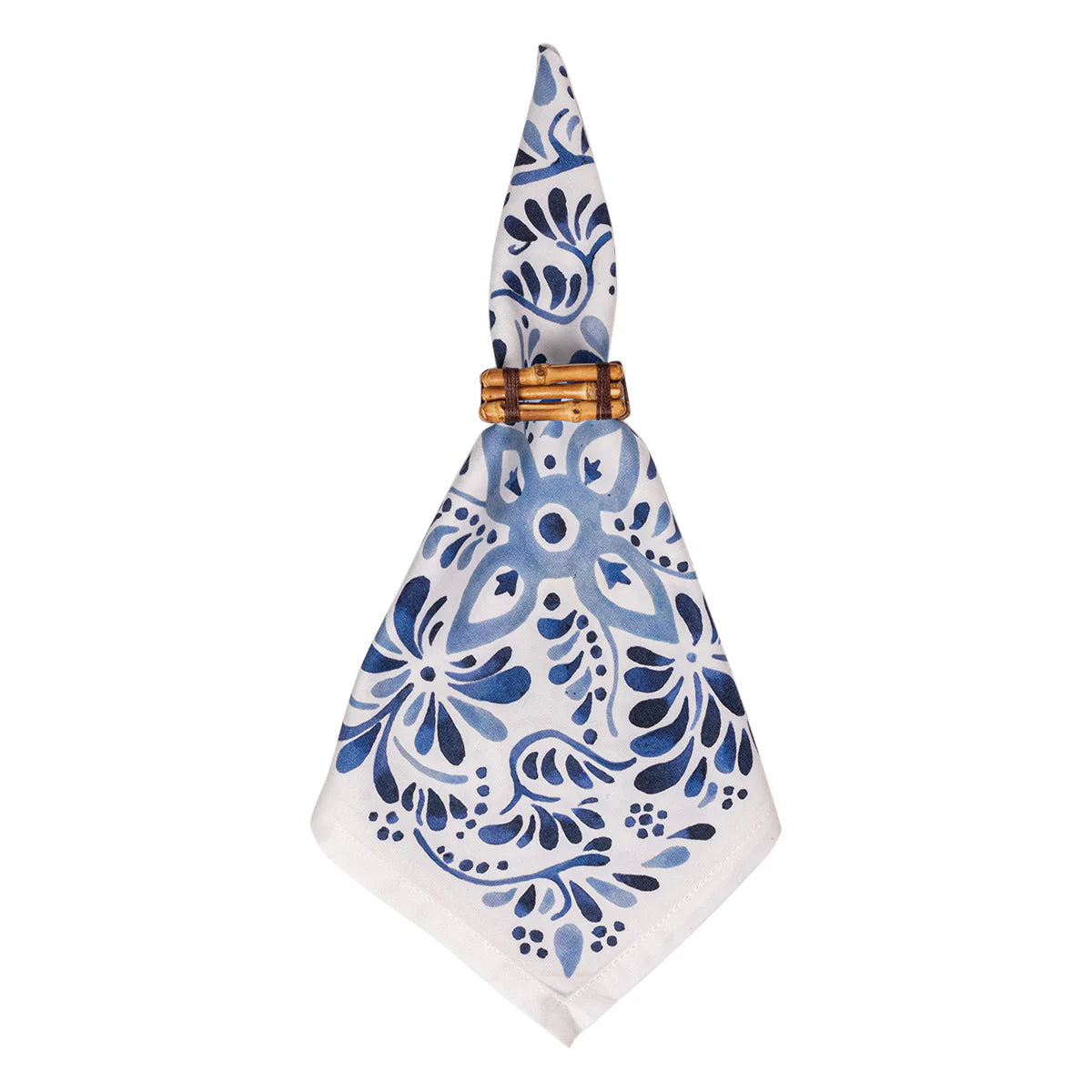 The Iberian Napkin Indigo by Juliska, a set of four white cloth napkins with blue floral patterns inspired by cobalt tiles, is neatly folded and secured with a wooden napkin ring.