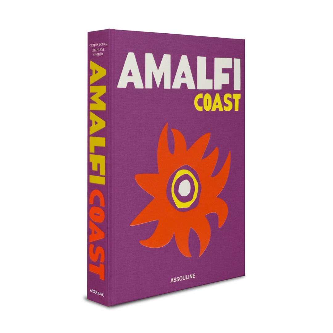 The Amalfi Coast Book by Assouline features bold white and yellow text on a purple cover with an abstract orange and yellow floral design; the author and Assouline appear on the spine and cover.