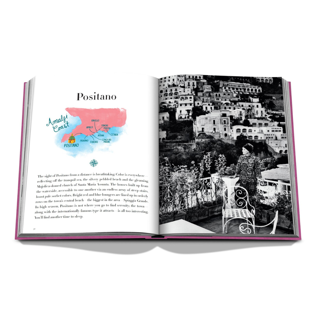 An open Assouline Amalfi Coast Book reveals a watercolor map marked "Amalfi Coast" and "Positano" on the left page, with a black-and-white hillside town photo featuring a person on a terrace on the right.