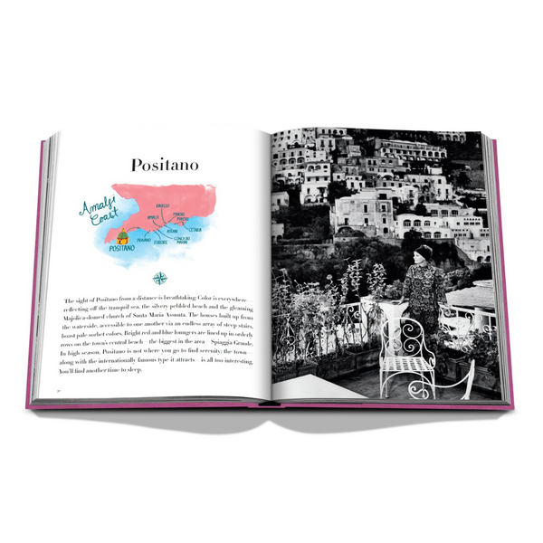 An open Assouline Amalfi Coast Book reveals a watercolor map marked "Amalfi Coast" and "Positano" on the left page, with a black-and-white hillside town photo featuring a person on a terrace on the right.