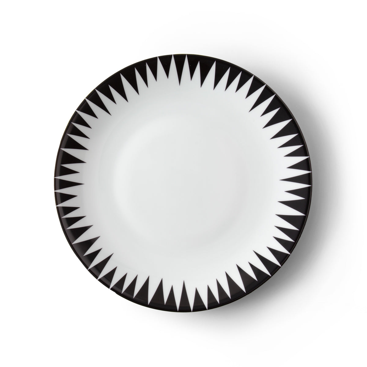 The Punk Dinnerware by Molecot features a round white Limoges porcelain plate with a bold black geometric triangle pattern radiating from the rim, creating a striking starburst effect—an ideal piece of modern tableware.