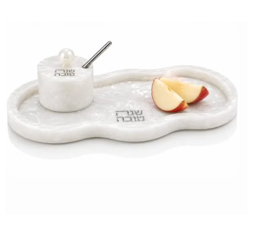 The Resin Curved Simanim Tray Set by Waterdale Collection features a white marble tray with Hebrew text, holding a matching round resin honey dish with lid and spoon, accompanied by two apple slices. The arrangement is presented in a clean, minimalist style against a white background.