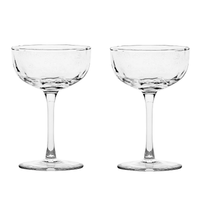Two clear, empty Puro Cocktail Coupe glasses by Juliska, each featuring a short stem and wide, shallow bowl, are placed side by side on a plain white background—an ideal choice for serving elegant cocktails or gifting as a beautifully boxed set.