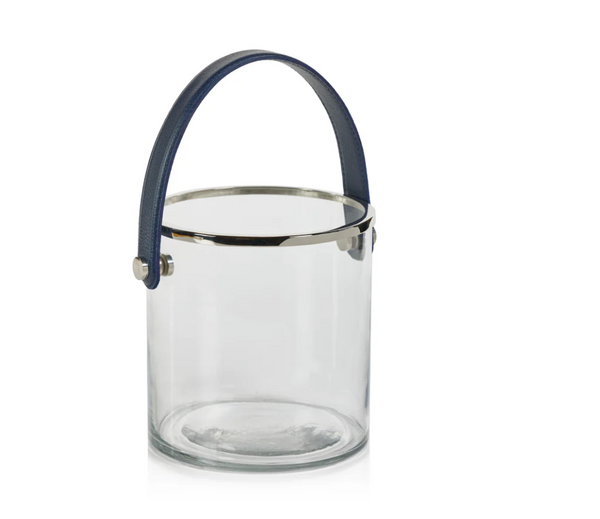 The Zodax Laguna Ice Bucket features a clear cylindrical glass body, silver metal rim, and dark blue leather handle—a stylish champagne bucket photographed against a white background.