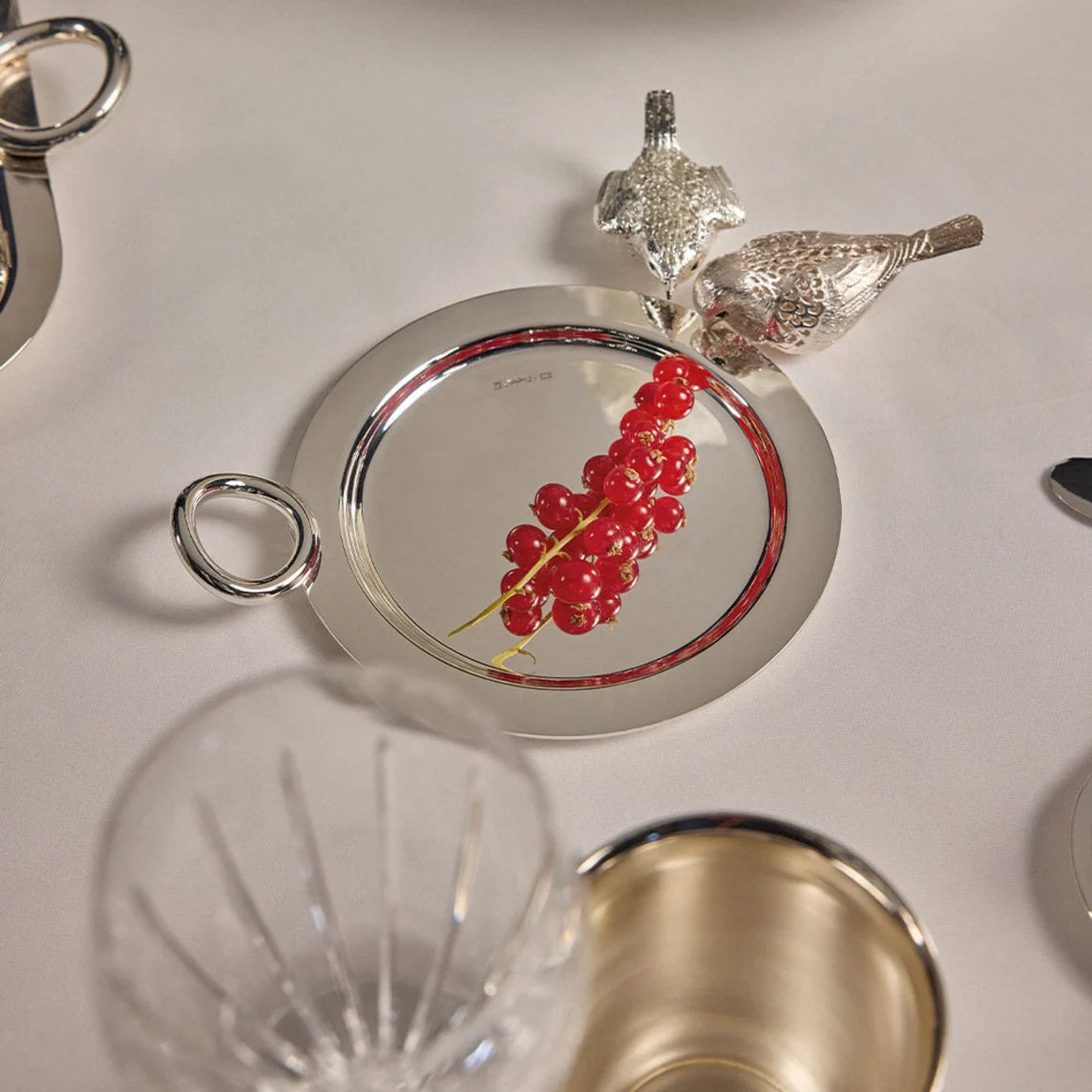 Round silver-plated Vertigo Christofle Silver-Plated Bottle/Carafe Coaster with a ring handle, topped with two small silver bird figurines and a sprig of red currants.