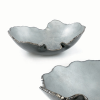Here’s a rewrite of the sentence using your product data: Two artistic Mapa Grey & Silver Trim Bowls by Gardeco feature matte-finished grey ceramic, uneven wavy edges, and metallic detailing that evoke an organic, handcrafted look reminiscent of Regina Medeiros artisan glassware. One bowl is fully visible while the other appears partially in the foreground, both showcasing striking artistry inspired by fine Brazilian design.
