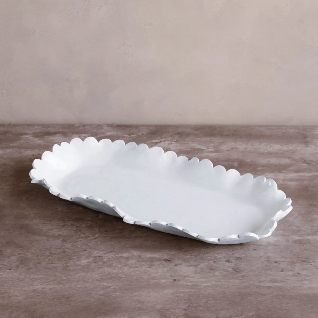 The Beatriz Ball Vida Colette Melamine Platter White - Large features elegant scalloped edges, resting on a brown textured surface against a beige wall—ideal for stylish presentations at any gathering.