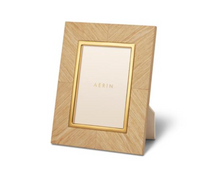 A Marcello Frame Oak by Zodax with a gold inner border stands upright. The frame features a simple, modern design and displays a card with “AERIN” printed on it.