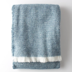 The Four Sided Pinstripe Fringe Throw by A Soft Idea is a folded blue and white wool blend with a subtle houndstooth pattern and white fringe on one end, shown against a plain white background.