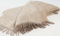 A luxuriously soft, beige Diana Mohair Throw by Mantas Ezcaray with long fringes at the ends is neatly folded on a white background, evoking the elegance of a classic blanket.