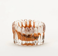 The Splash Catchall Bowl by Gary Bodker, crafted from clear glass with vertical ridges and a wavy rim, features distinctive brownish-orange accents on the inside. Set against a plain white background, its artisanal design and meticulous detailing evoke the charm of a handcrafted decorative dish.