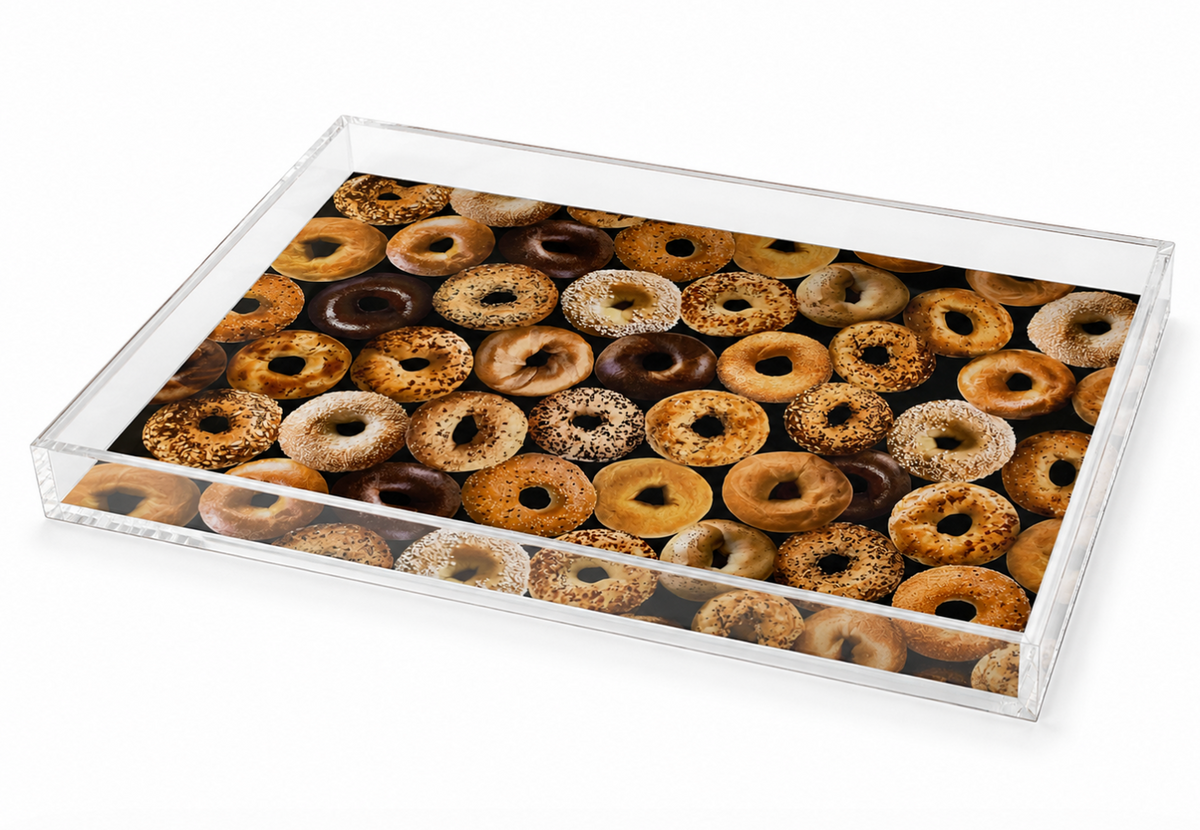 Bring festive flair to your next holiday breakfast with the Eye Candy Bagel Tray Wide - Bagel Print, a clear rectangular acrylic tray featuring a vibrant pattern of assorted bagels—including plain, sesame, poppy seed, and everything—arranged closely together against a white background. Perfect for serving as a cheerful bagel tray.