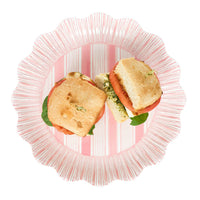 A sandwich with tomato, mozzarella, and greens, cut in half and served on a Juliska Cabana Stripe Melamine Dinnerware plate in coral.