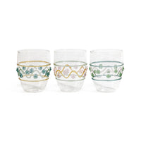 The Zodax Festa Tumbler Set of 3 features clear soda lime glass tumblers in green, amber, and pink tones, each adorned with wavy colored lines and small beads encircling the middle; the gold tumbler has pink flower accents.
