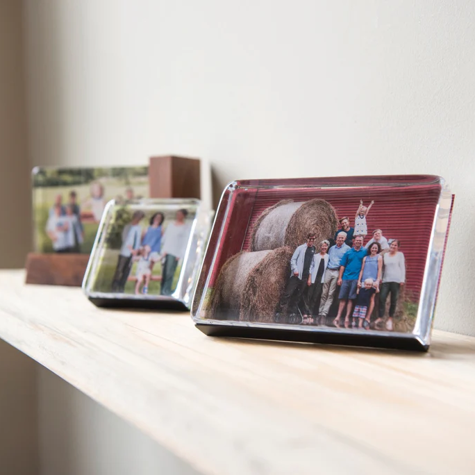Framed photographs on a white shelf against a plain wall