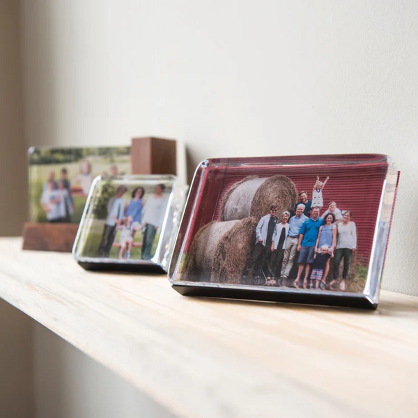 Framed photographs on a white shelf against a plain wall