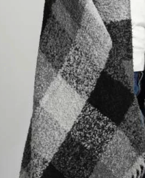 A close-up of a person wearing the Bristol Boucle Throw in Grey/Black by Alicia Peru Home draped over a white top and blue jeans.
