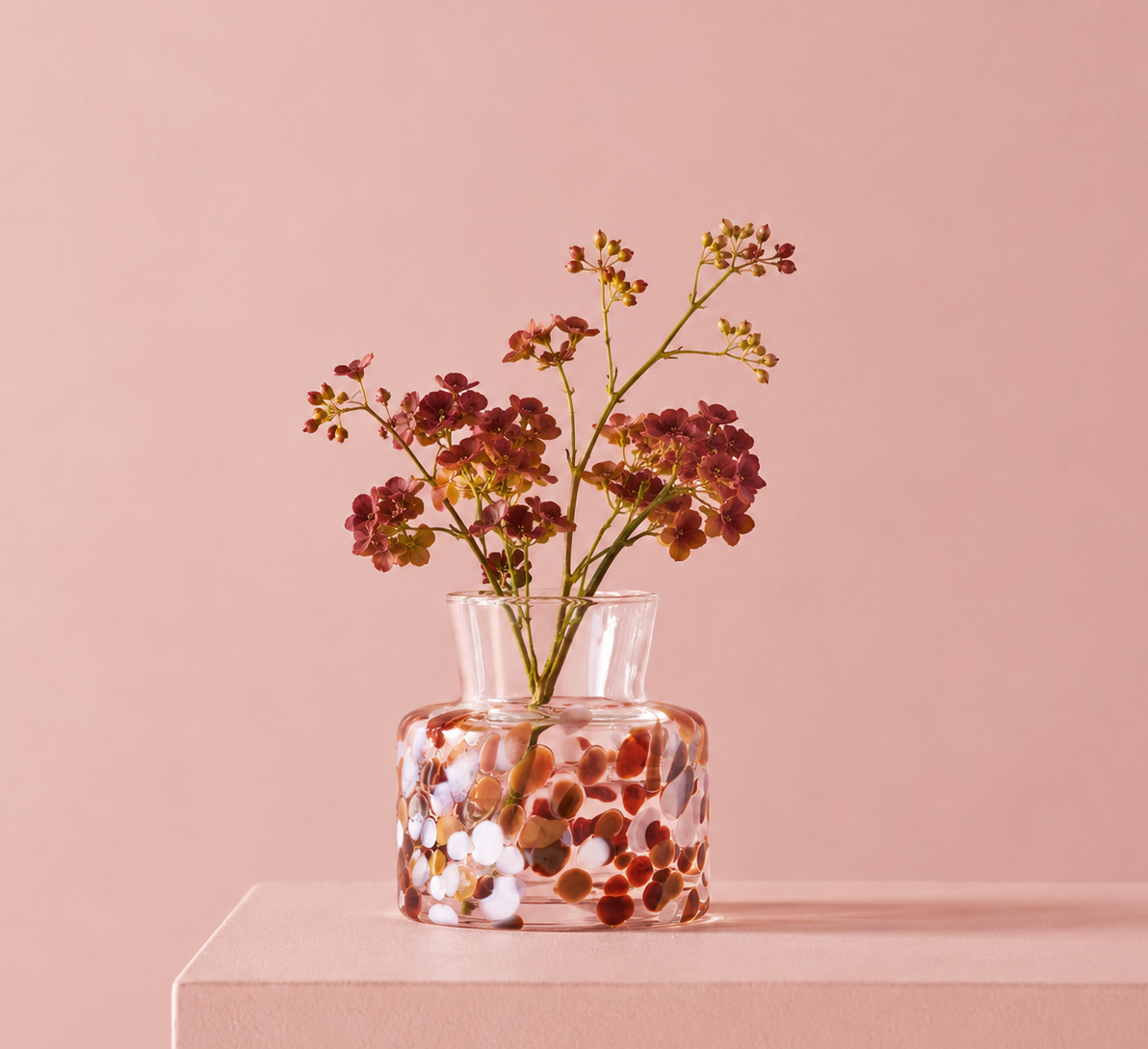 Small Meadow Vase Fall by Orrefors Kosta Boda with a multi-colored speckled pattern containing a stem of small dark red flowers.