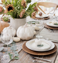 An elegant autumn tablescape featuring white Capiz Pumpkin White decor, a flower arrangement, and woven placemats.