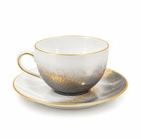 Marie Daâge Horizon Gold hand-painted porcelain teacup and saucer featuring a grey gradient wash, gold splatter detailing, and gold rims.
