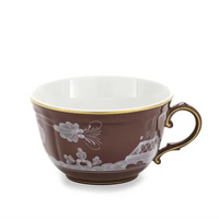 A brown porcelain teacup from the exquisite Ginori 1735 Oriente Italiano Castagna collection, featuring a gold rim and handle and adorned with white floral and landscape patterns. Expertly crafted in Italy, the cup is displayed against a white background.