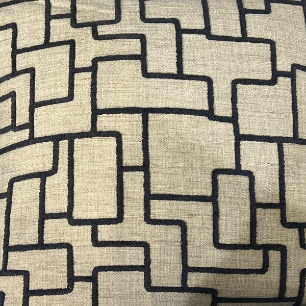 A close-up of Decor Fifty-Five’s Shapeshifter Pillow Black & Tan shows its beige fabric with interlocking, irregular rectangles in dark thread, creating a maze-like contemporary pattern.