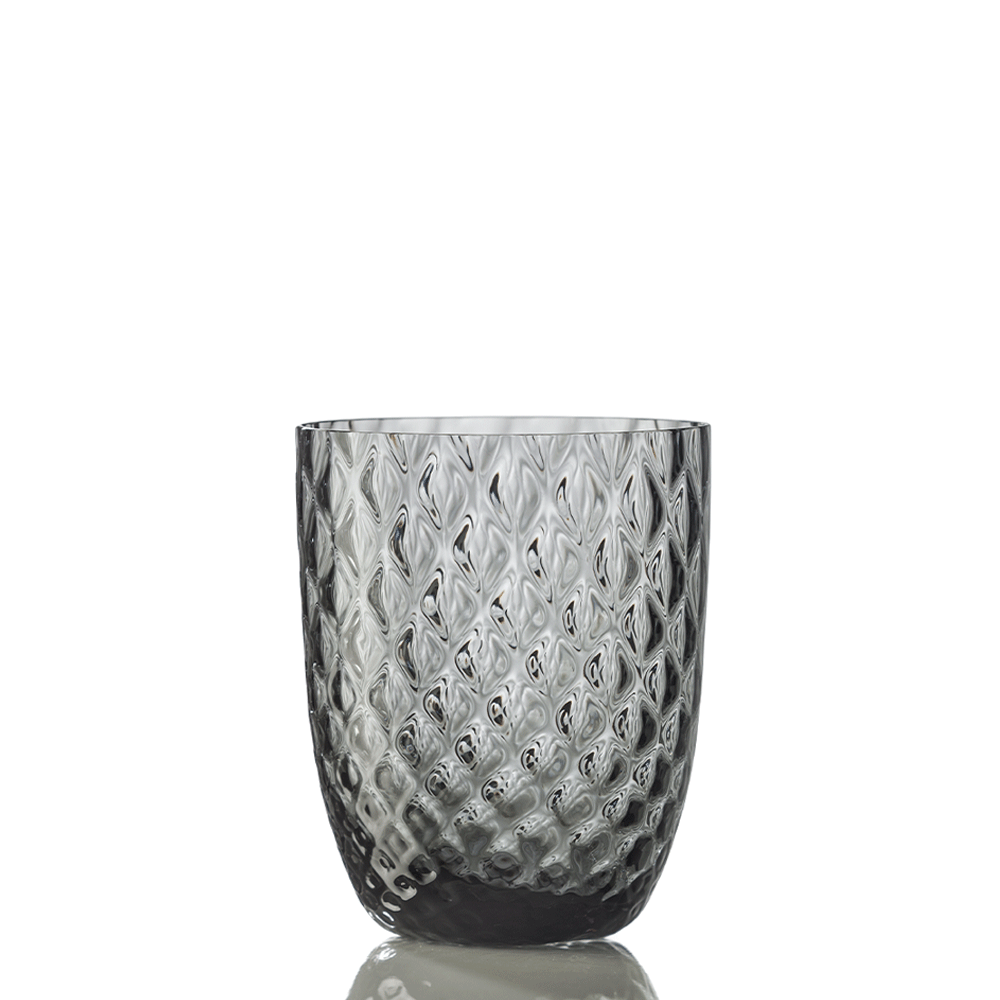 An Idra Grey Balloton Tumbler by Nason Moretti with a clear, diamond-textured glass design stands on a white surface, reflecting light.