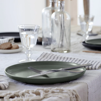 A Pacifica Dinnerware Artichoke plate from Casafina/Costa Nova, accompanied by a fork and knife, rests elegantly on a set table with a glass of water, striped napkin, and glass bottles atop a textured white tablecloth—a beautiful showcase of luxury tableware.