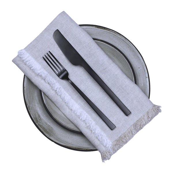 Two stacked ceramic plates topped with a Hogar Frayed Edge Linen Napkin by Linen Casa in light gray. A black fork and knife rest on the napkin, creating a simple, elegant table setting.