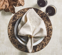 Table setting with a marble-patterned charger, gray and white plates, a beige embroidered napkin accented by the Kim Seybert Mineral Napkin Ring set of 4 in Brown, and two glasses of a dark beverage, viewed from above on a light surface.