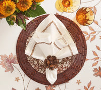 Table setting with a brown woven placemat, a floral-patterned plate, the Kim Seybert Filament Napkin Set of 4 in White & Brown secured with a wooden flower napkin ring, sunflowers in a vase, and two amber-colored drinks on an elegant floral tablecloth.