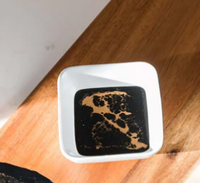 The Painted Dip Bowl - Black Ember by Lynn & Liana Serveware holds dark soy sauce on a wooden surface, sunlight casting shadows across the scene.