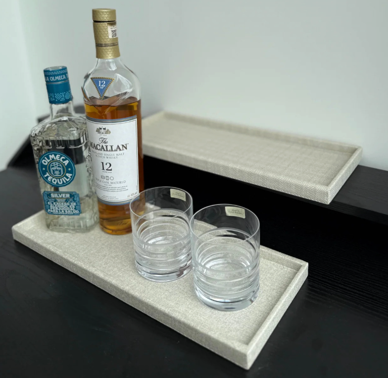 A Bold Decor Victoria Long Rectangle Serving Tray holds a bottle of Olmeca Silver tequila, Macallan 12 whisky, and two empty glass tumblers on a dark surface, with another empty tray placed behind it.