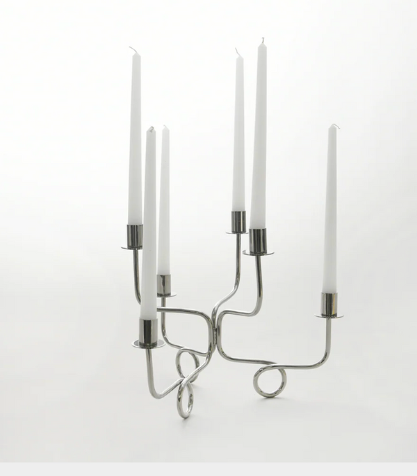 The Together Candelabra - Silver by Byaas, featuring a geometric looped base and minimalist design, displays six tall white taper candles against a plain white background.