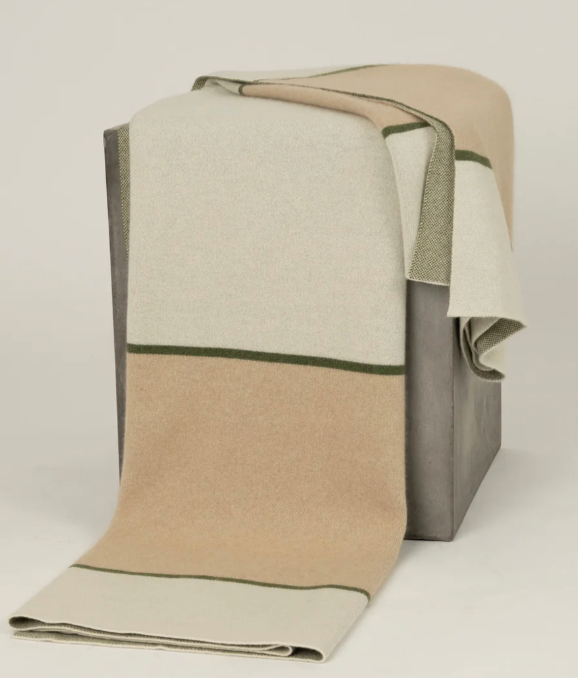 The Hangai Mountain Textiles Modern Minimalist Cashmere Throw - Olive, featuring beige, cream, and light green stripes, is draped over a gray rectangular box against a plain background.