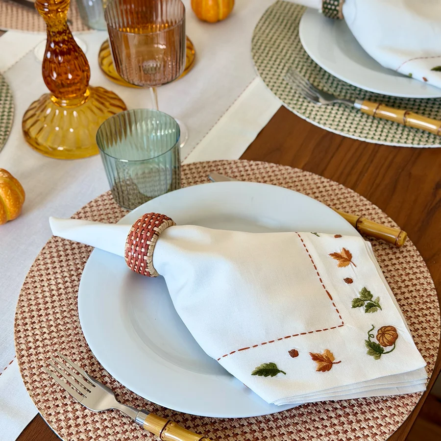 Celebrate the season with a fall-themed table setting featuring Bodrum’s Autumn Medley Napkin Set of 4. Pair your white plates with these embroidered napkins, woven napkin rings, gold flatware, and colored glasses. Mini pumpkins and amber candle holders accent the wooden table, all beautifully complemented by an embroidered table runner for a warm and inviting touch perfect for Thanksgiving entertaining.