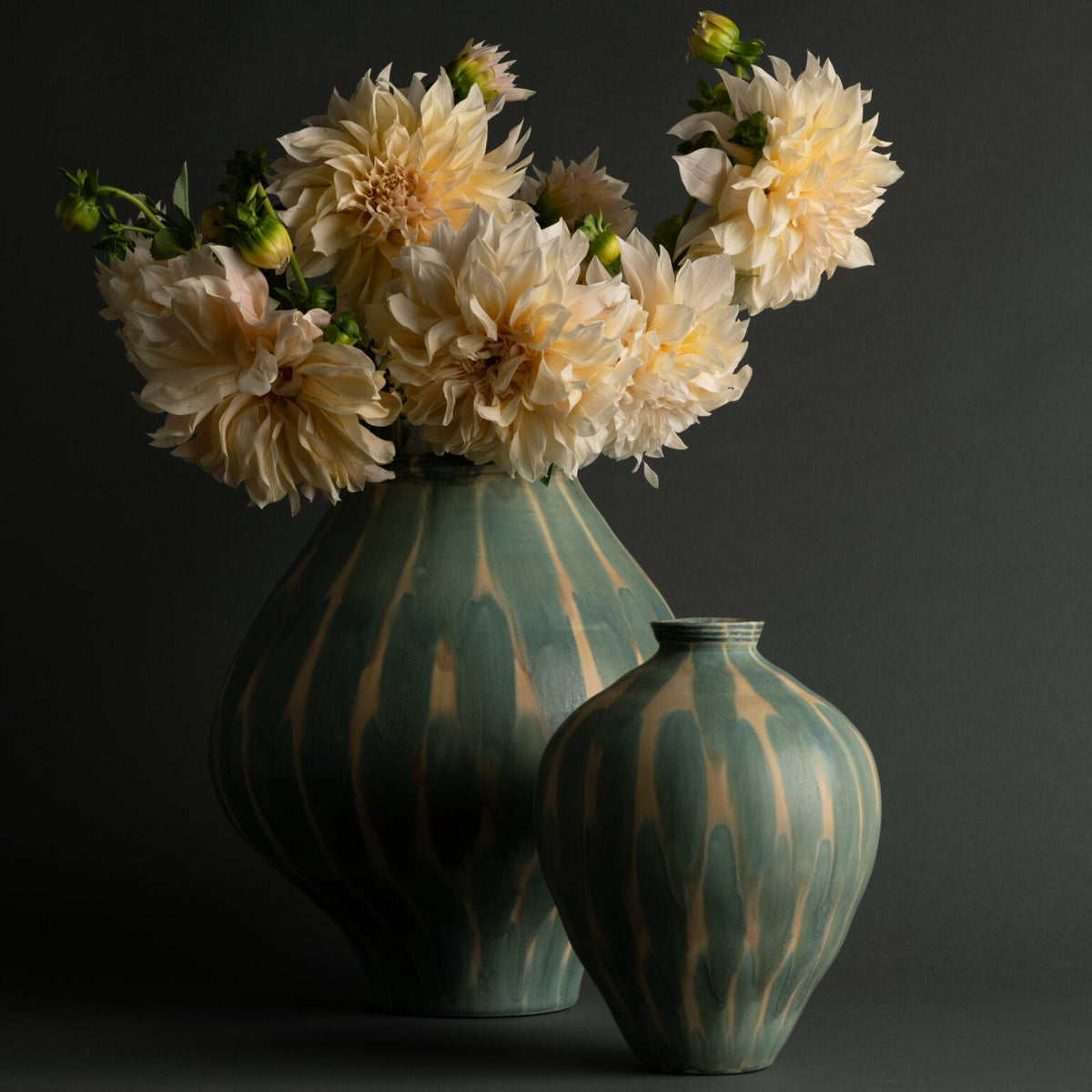 Two Jace Vases from FlowDecor Inc.—one large and one small—feature elegant ceramic construction with green and beige patterns. The larger decorative vase displays a bouquet of pale, full-bloom dahlias, all set against a dark, neutral background.