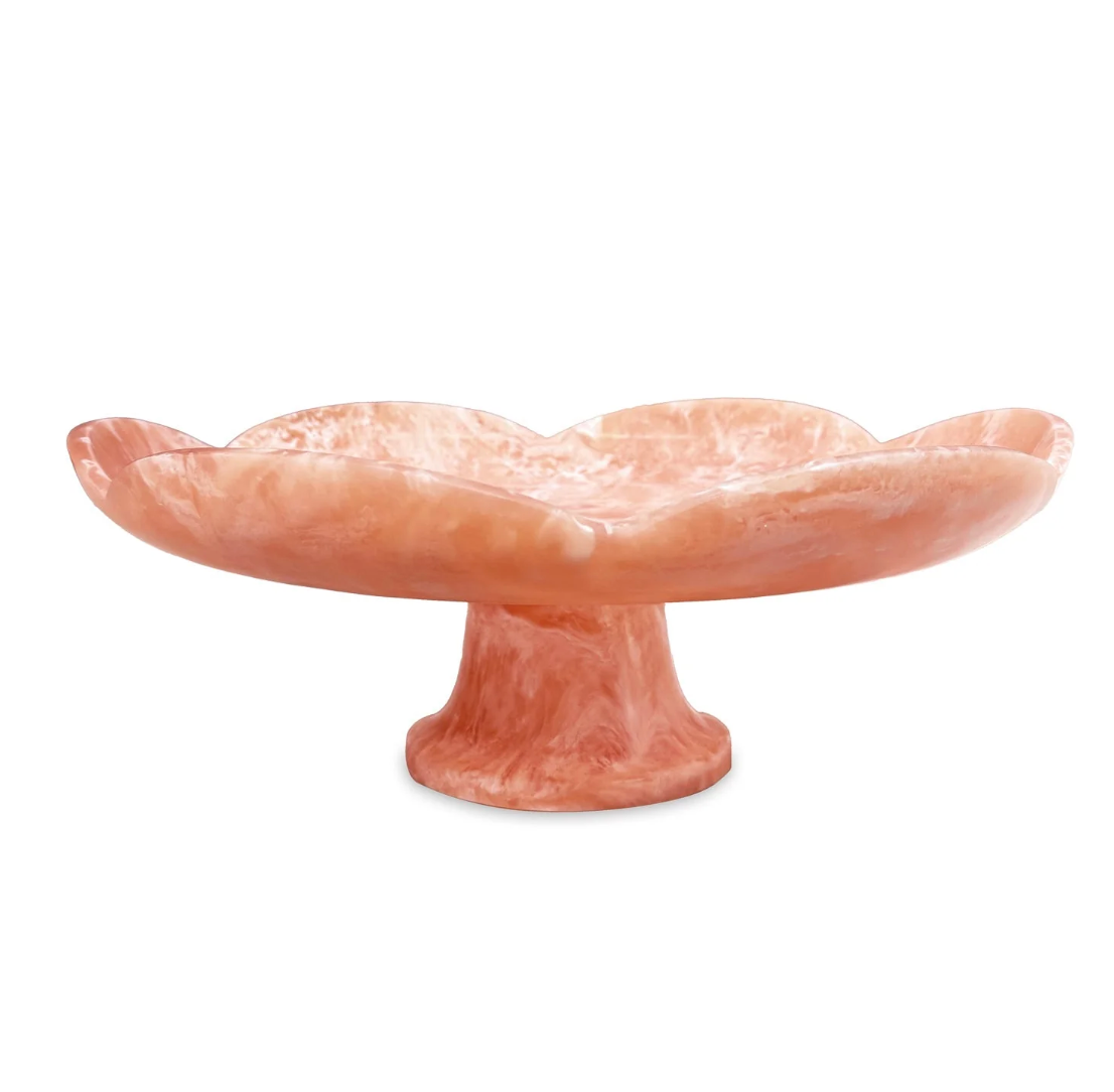 The Beatriz Ball Resin Amelia Pedestal Cake Plate in peach features a marble pattern, scalloped flower-like edge, and wide shallow dish—perfect as a handcrafted tableware accent or serving platter.
