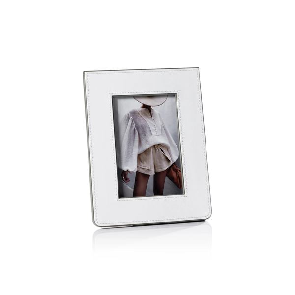 The Zodax Napoli Leather Frame White & Grey stylishly displays a photo of a person in a textured blouse, beige shorts, and wide-brimmed hat, with their face partially out of view.