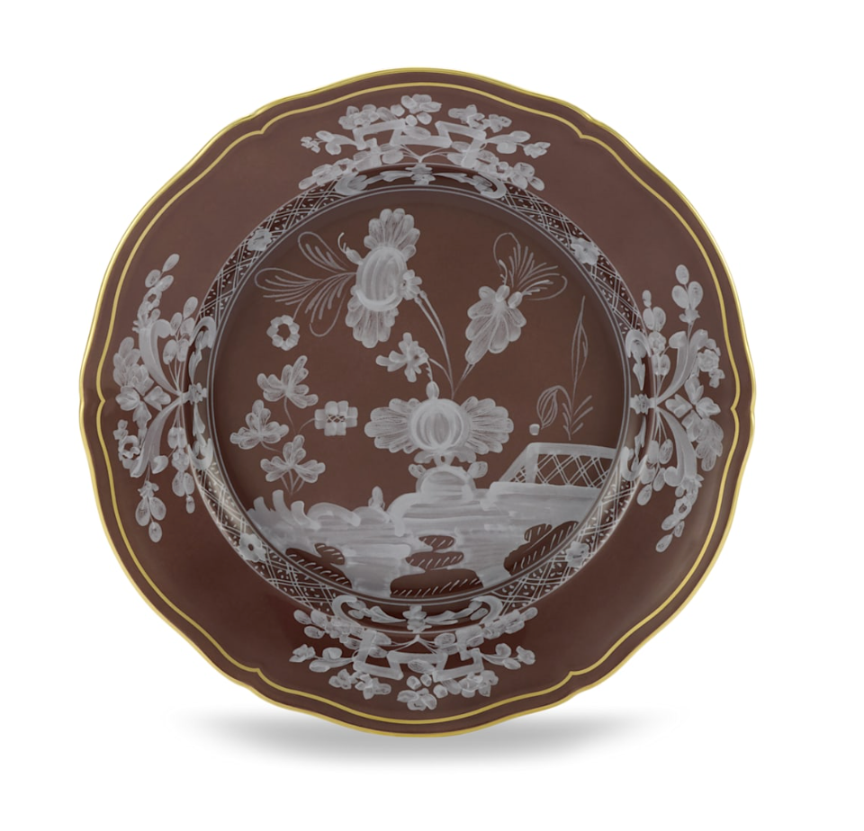The Oriente Italiano Castagna plate by Ginori 1735 features a brown hue, scalloped edge, gold trim, and intricate white floral and landscape designs—a decorative Italian-crafted piece for your tableware collection.