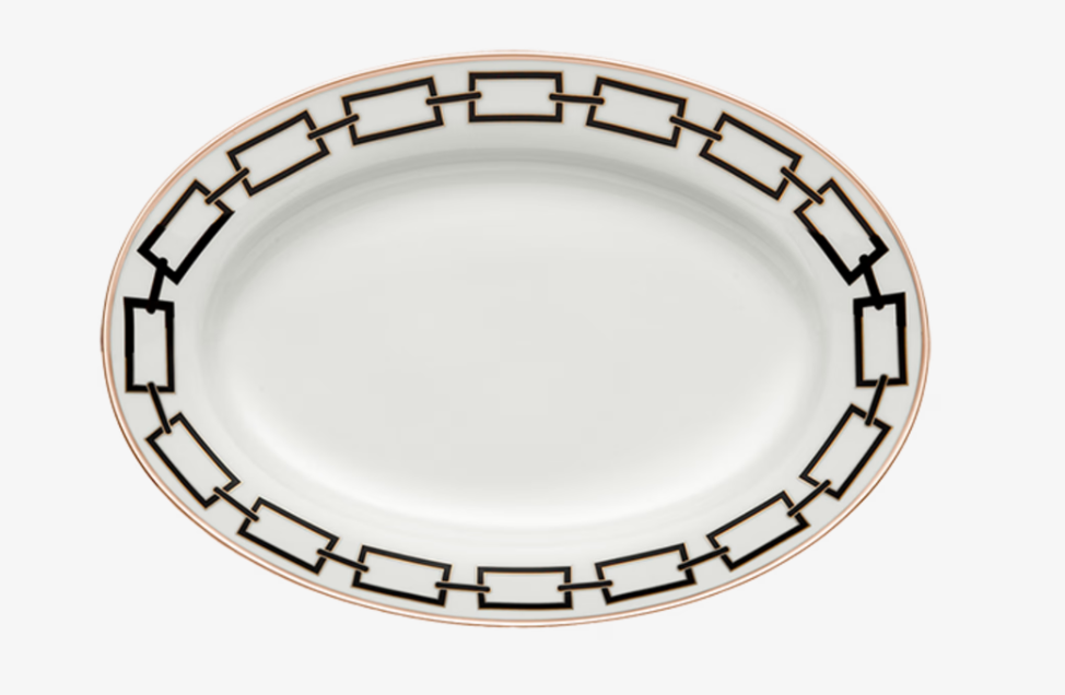 The Catene Nero Dinnerware by Ginori 1735 features an oval white plate adorned with a black geometric chain pattern around the rim and accented by a thin gold border on the edge.