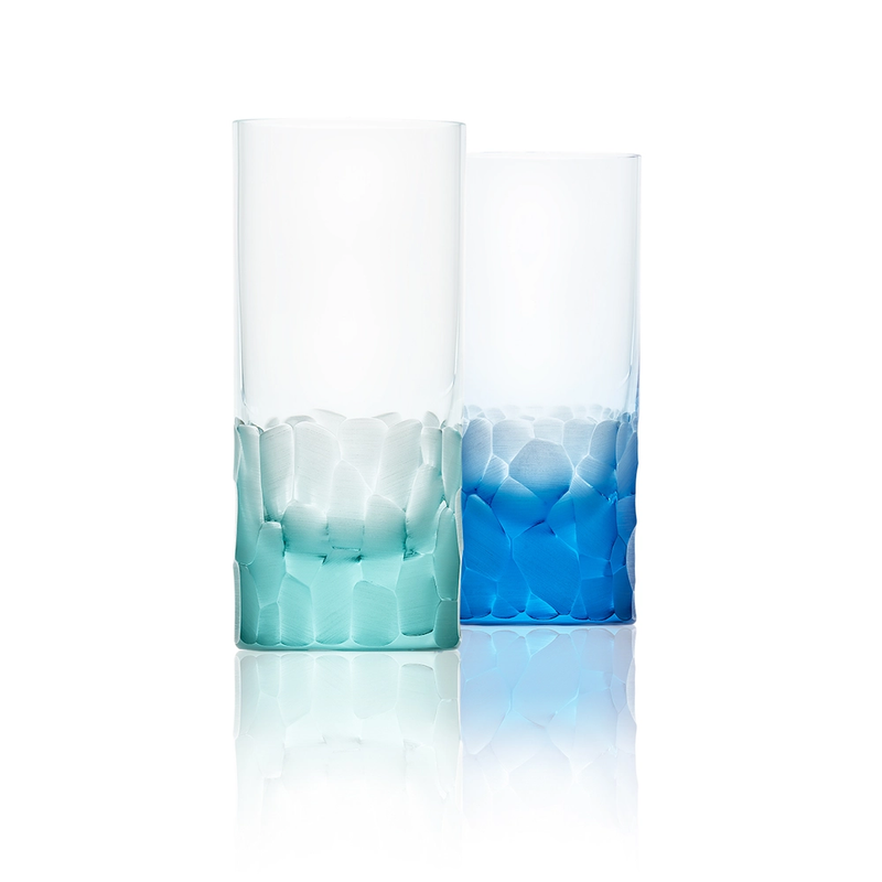 Two Pebbles Highball 400ml glasses by Moser, hand-blown from lead-free Czech crystal—one with a turquoise gradient, the other blue—feature textured faceted bases, shown on a white background with subtle reflection.