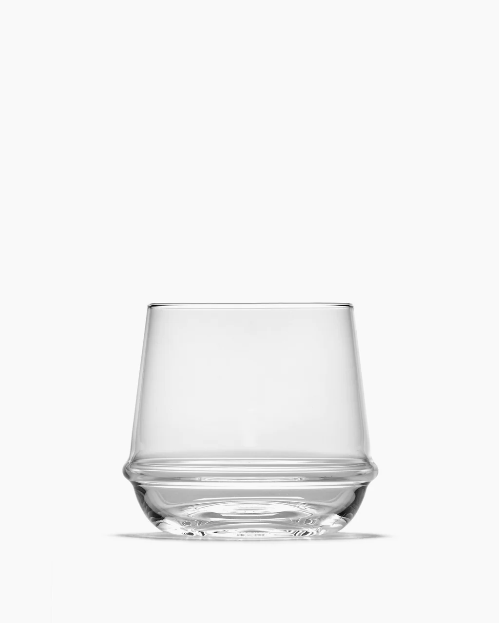 A clear Dune Whiskey Glass by Serax, empty and short with a wide base and a subtle ridge near the bottom, set against a plain white background.