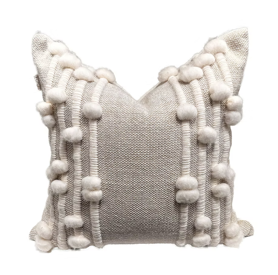 The Decorum Wooly Bumps Pillow - Sand / White is a handcrafted square cushion with textured beige fabric, vertical rows of fluffy white pom-poms, and woven ridges—perfect for adding cozy style to any home.