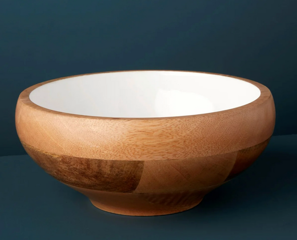 The Mayan Wood Footed Bowl - Medium by Be Home features a smooth, light brown exterior and a glossy white interior, showcased against a dark blue background.