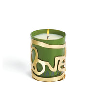 The Amber Sakai Love Candle - Amour features a green candle in a 24K gold-plated holder adorned with the word “love” in elegant cursive script, lit with a gentle flame against a white background.